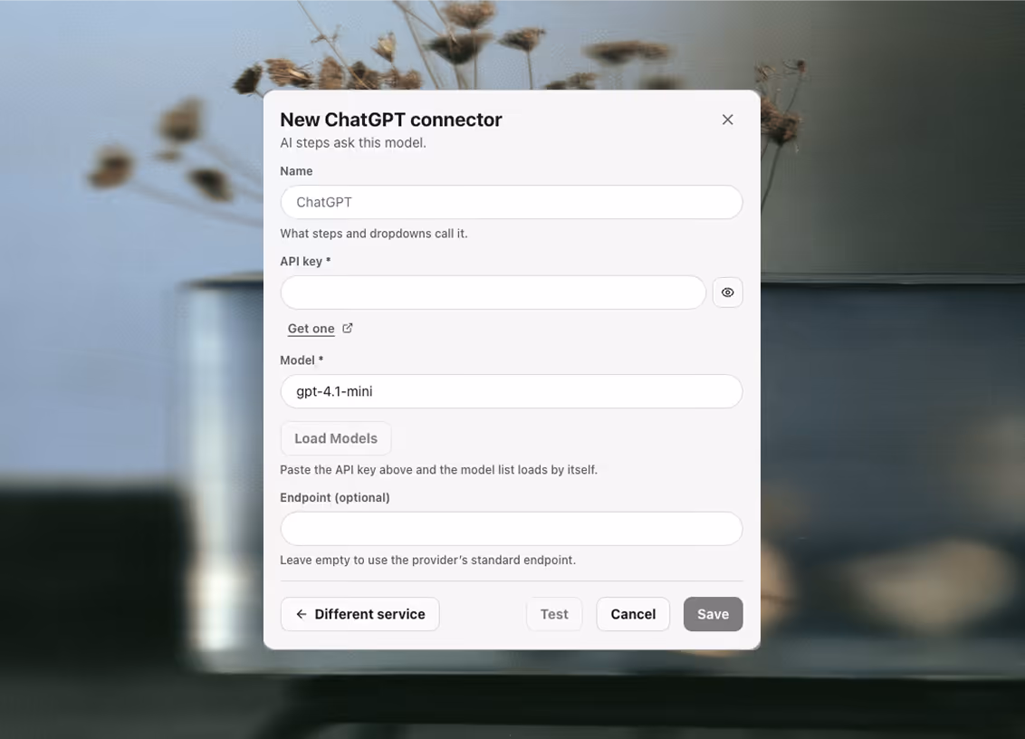 The new-connector dialog for ChatGPT: a display name, an API key field with a reveal control and a Get one link, a model field with a Load Models button that fills the list once the key is pasted, and an optional endpoint left empty to use the provider's standard one. Test, Cancel and Save sit at the foot, with Different service beside them.